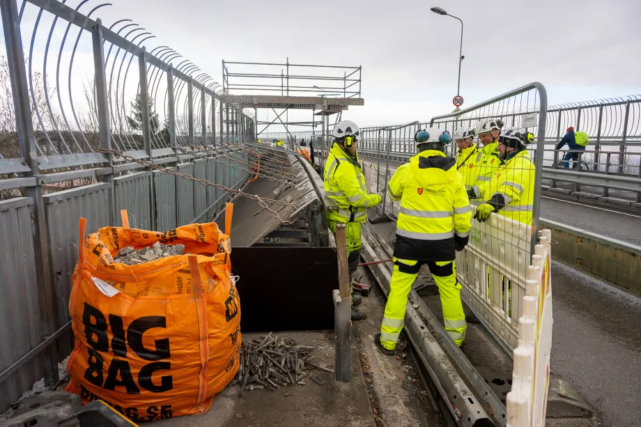 Arbeidere i gule klær jobber i gangveien på Tromsøbrua